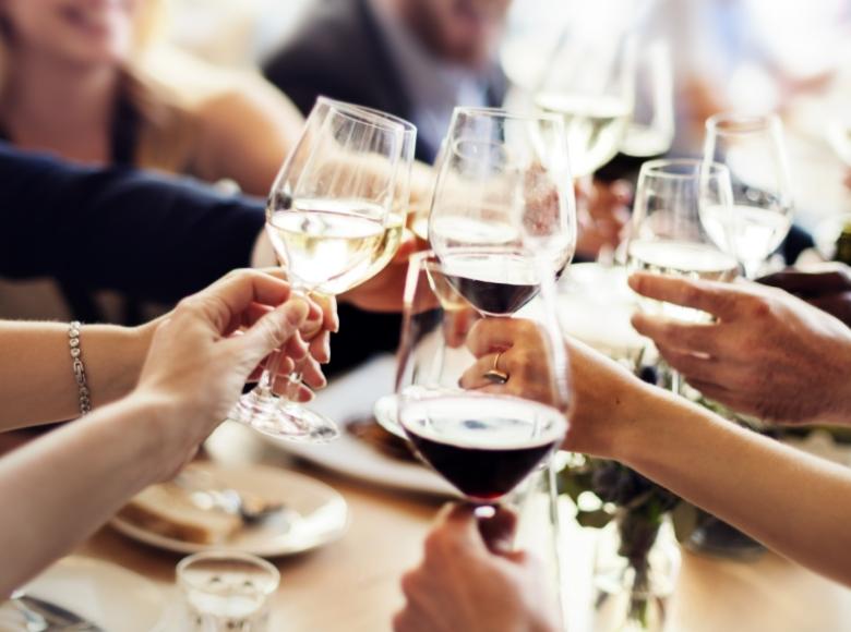 Persone brindano con bicchieri di vino durante un pasto conviviale.
